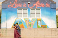 man in a suit kissing a woman in a maroon dress in front of the love is in the air mural in downtown Asheville