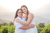 lesbian couple wearing white in the mountains looking at an engagement ring