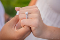 two women holding hands looking at an engagement ring with mountains in the background