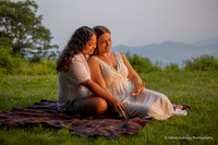 Lesbian couple cuddling on a blanket admiring engagement ring